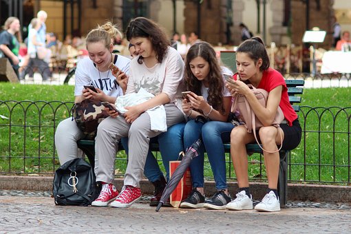 Small group of women sitting on a bench looking at their phones