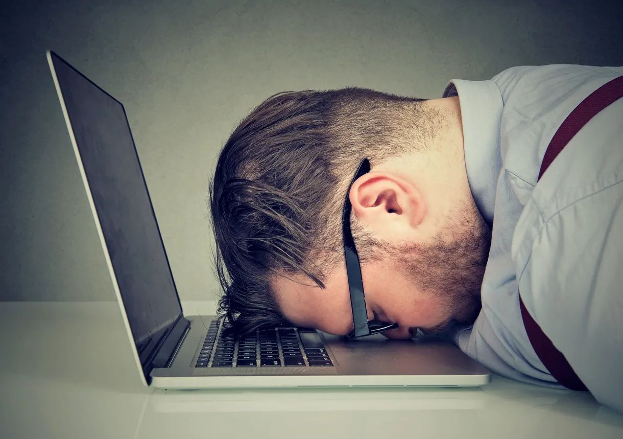 exhausted man asleep with head on laptop