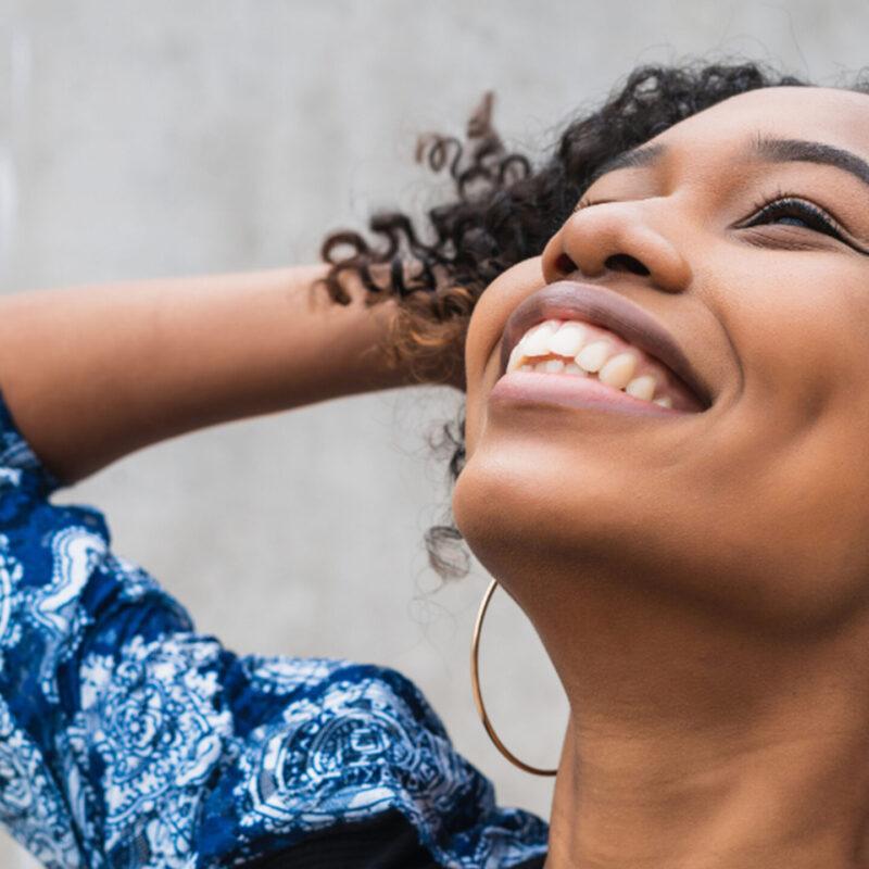 Black Woman Smiling and Dragging Hand Through Hair While Looking Up