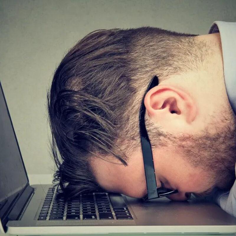 exhausted man asleep with head on laptop