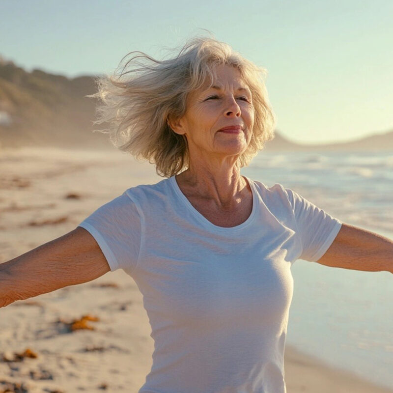 Older Woman with Outstretched Arms Walking on Beach