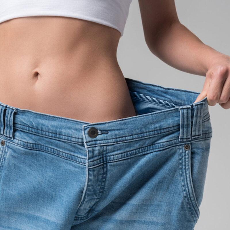 Woman Showing Her Weight Loss Pulling Larger Pants Away from Waist