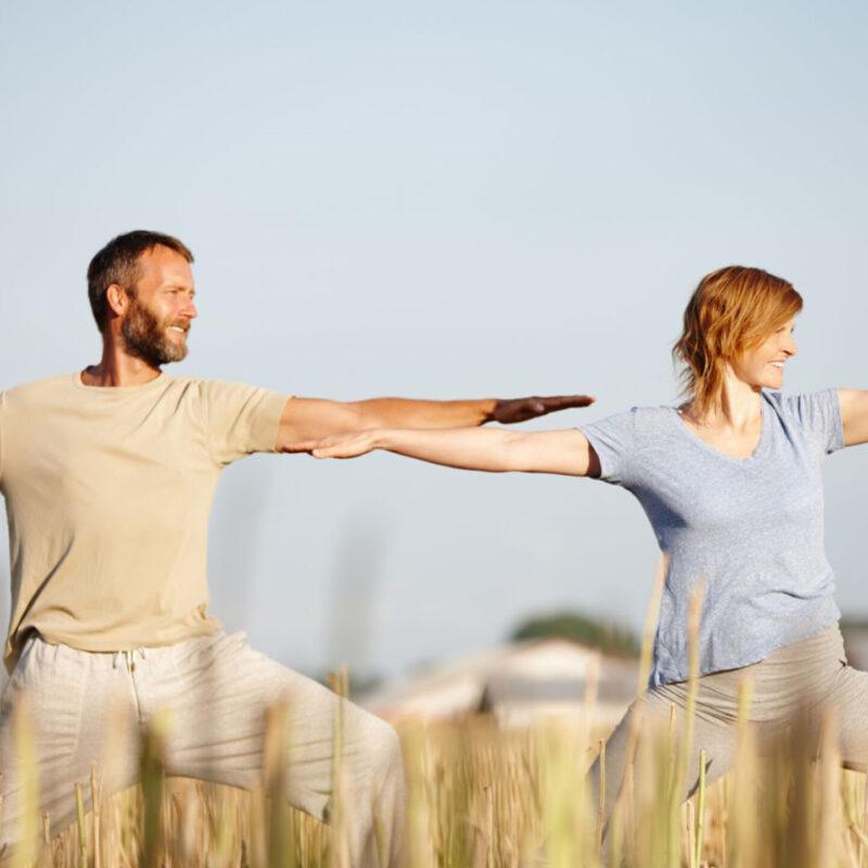 Middle-Age Couple in Field of Wheat Doing Yoga Stretches