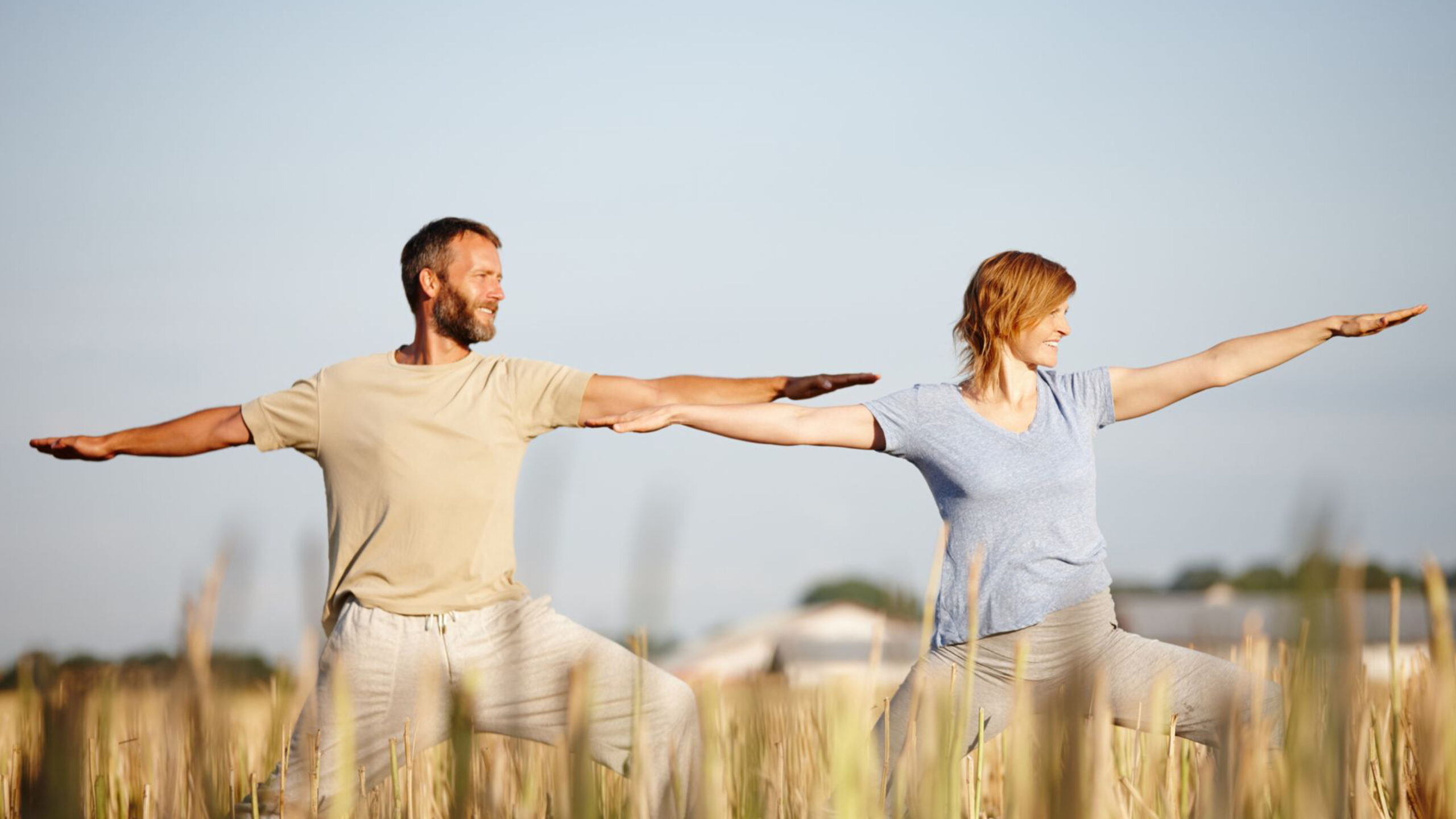 Middle-Age Couple in Field of Wheat Doing Yoga Stretches